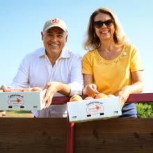 President Ángel Cabrera and Dr. Beth Cabrera holding boxes of peaches at Jaemor Farms